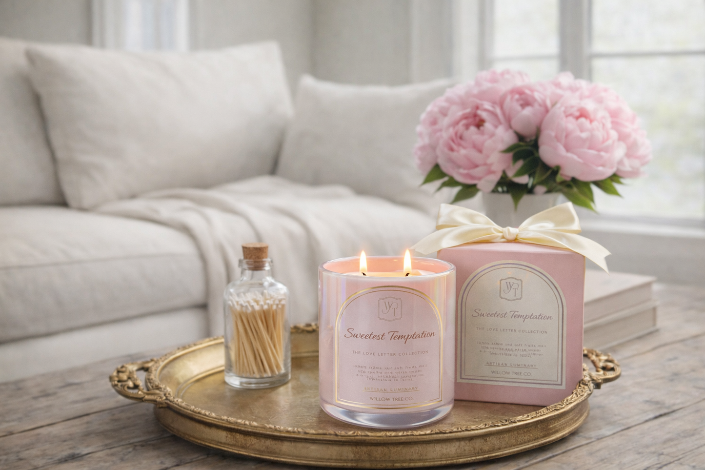 Pink candle and decorative items on a gold tray with a couch and flowers in the background