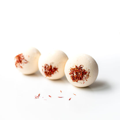 Three bath bombs with red flower petals on a white background