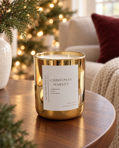 Christmas Market gold candle with two cotton wicks on a wooden table with evergreen decorations and warm Christmas lights.