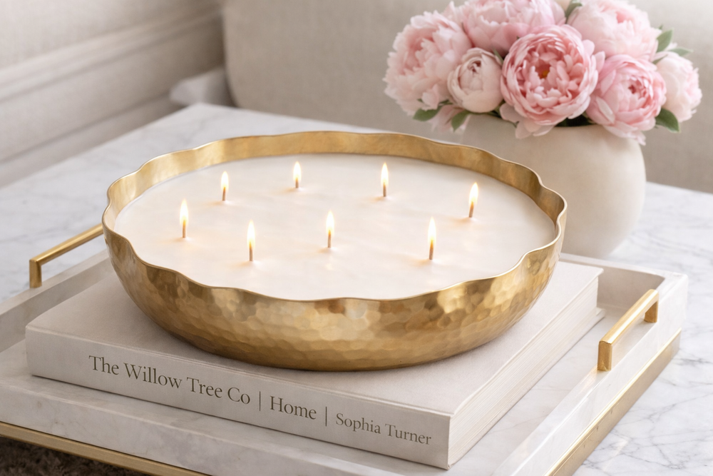 Gold bowl with lit candles on a book, next to pink flowers in a vase.