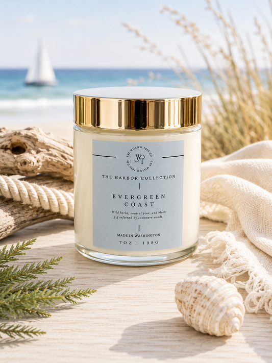 Luxury coastal candle with a soft ocean blue label styled beside driftwood, greenery, and seashells with an airy beach backdrop.