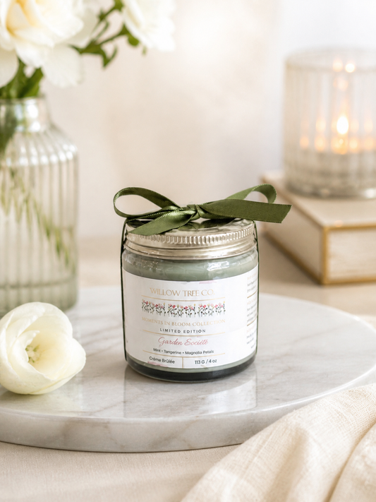 Jar of body cream with a green ribbon on a marble surface with flowers and candles in the background