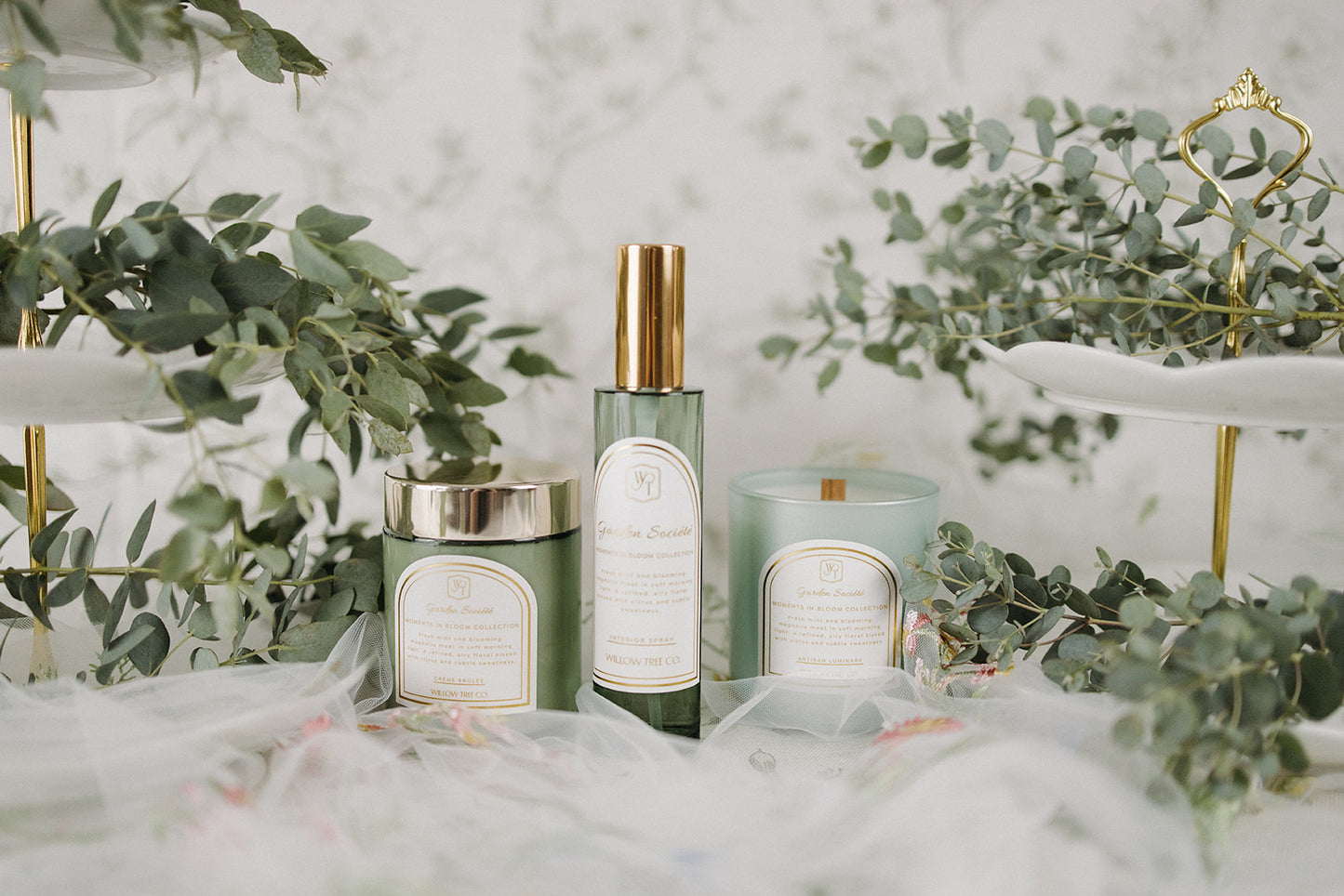 Body cream, interior spray, and candle with labels on a decorative surface with greenery
