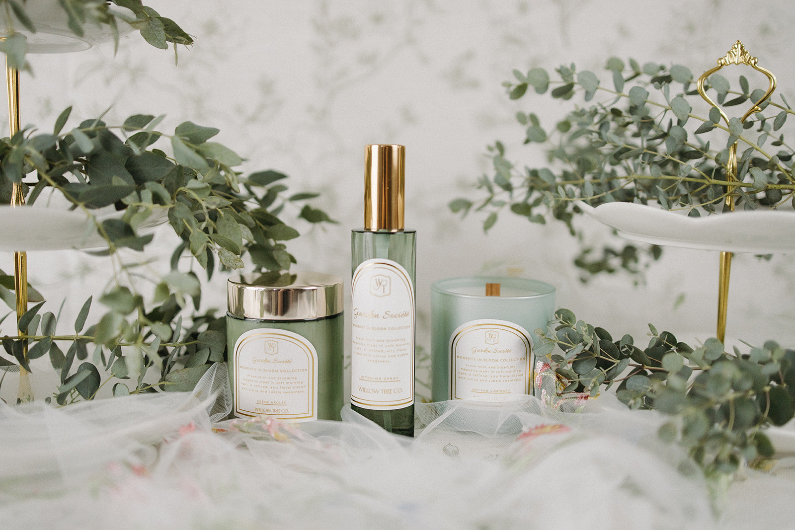 Body cream, interior spray, and candle with labels on a decorative surface with greenery