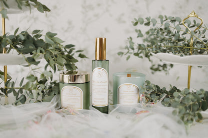 Body cream, interior spray, and candle with labels on a decorative surface with greenery