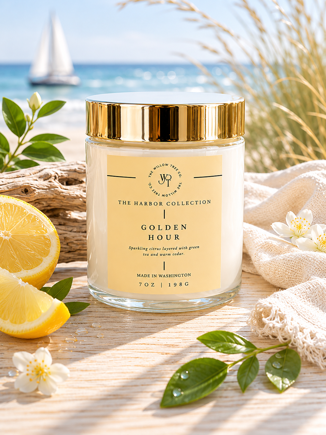 Candle jar labeled 'Golden Hour' from The Harbor Collection on a beach setting with lemons and flowers.