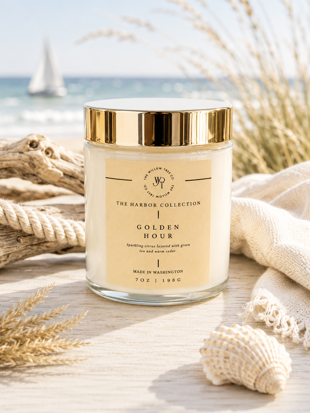 Luxury coastal candle with a warm wheat-colored label styled beside driftwood, rope, and seashells with an airy ocean backdrop.