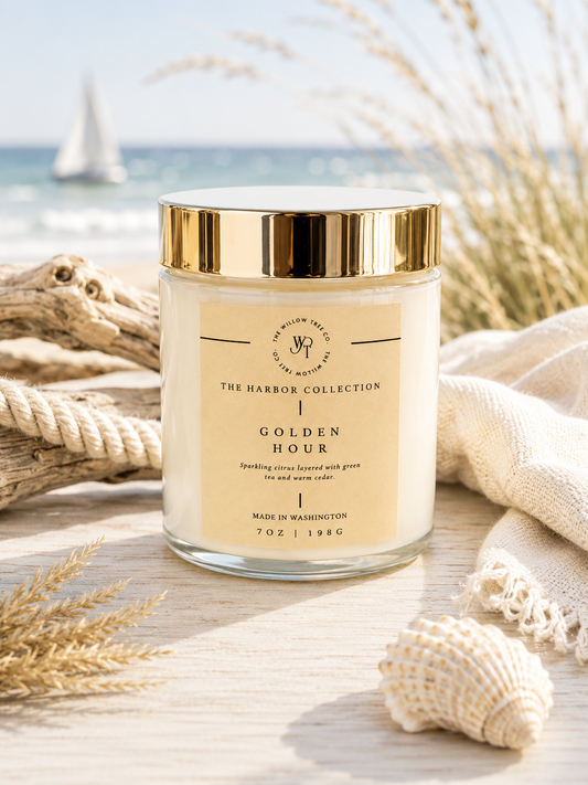 Luxury coastal candle with a warm wheat-colored label styled beside driftwood, rope, and seashells with an airy ocean backdrop.