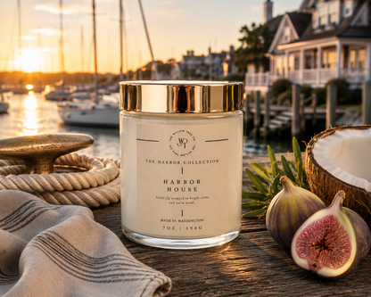 Candle labeled 'Harbor House' from 'The Harbor Collection' on a wooden surface with a sunset harbor background.