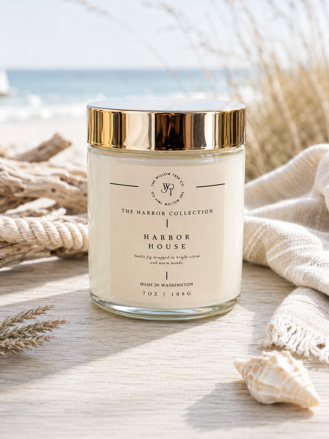 Luxury coastal candle with a soft sand-colored label styled beside driftwood, rope, and seashells with an airy ocean backdrop.
