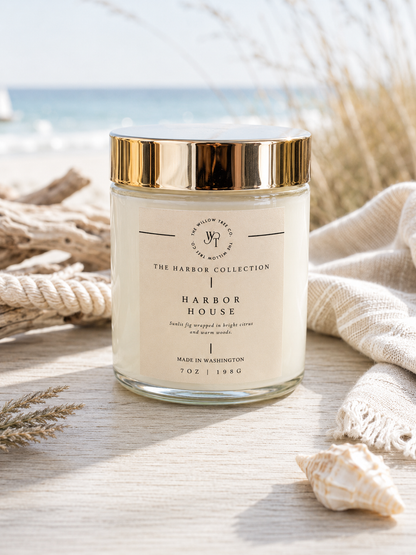 Luxury coastal candle with a soft sand-colored label styled beside driftwood, rope, and seashells with an airy ocean backdrop.