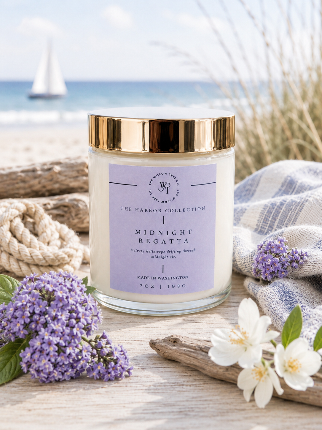 Candle with a purple label on a beach setting with flowers and rope.