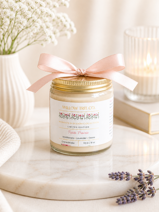 Body cream jar with a pink ribbon on a marble surface with lavender flowers and a book in the background.