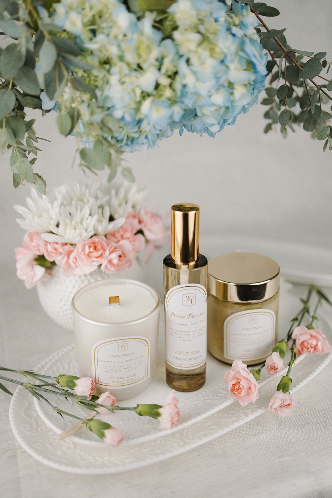 Candle, interior spray, and body cream on a tray with flowers in the background
