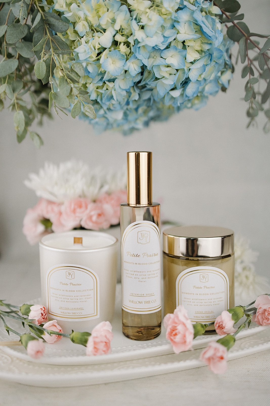 Candle, interior spray, and body cream with floral and eucalyptus decorations on a white surface.