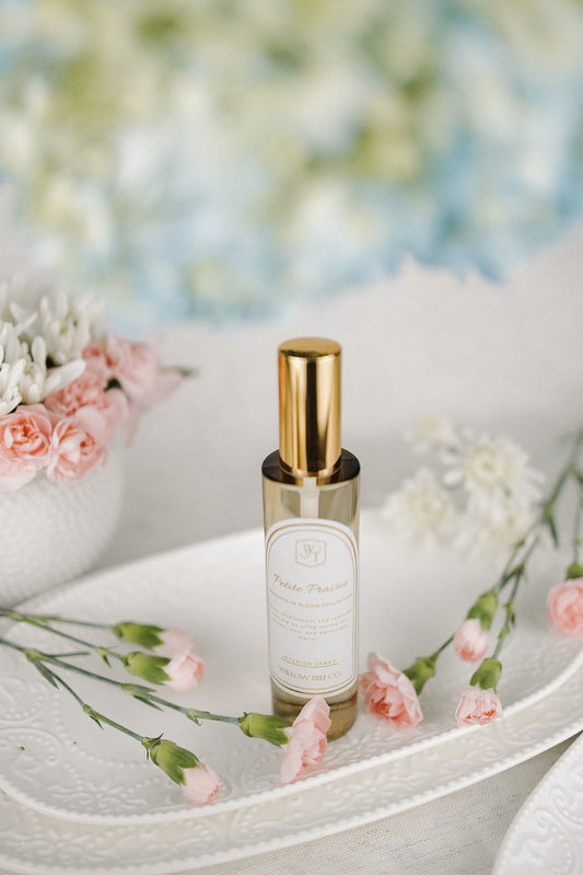 Small bottle of interior spray with gold cap on a white surface with flowers in the background