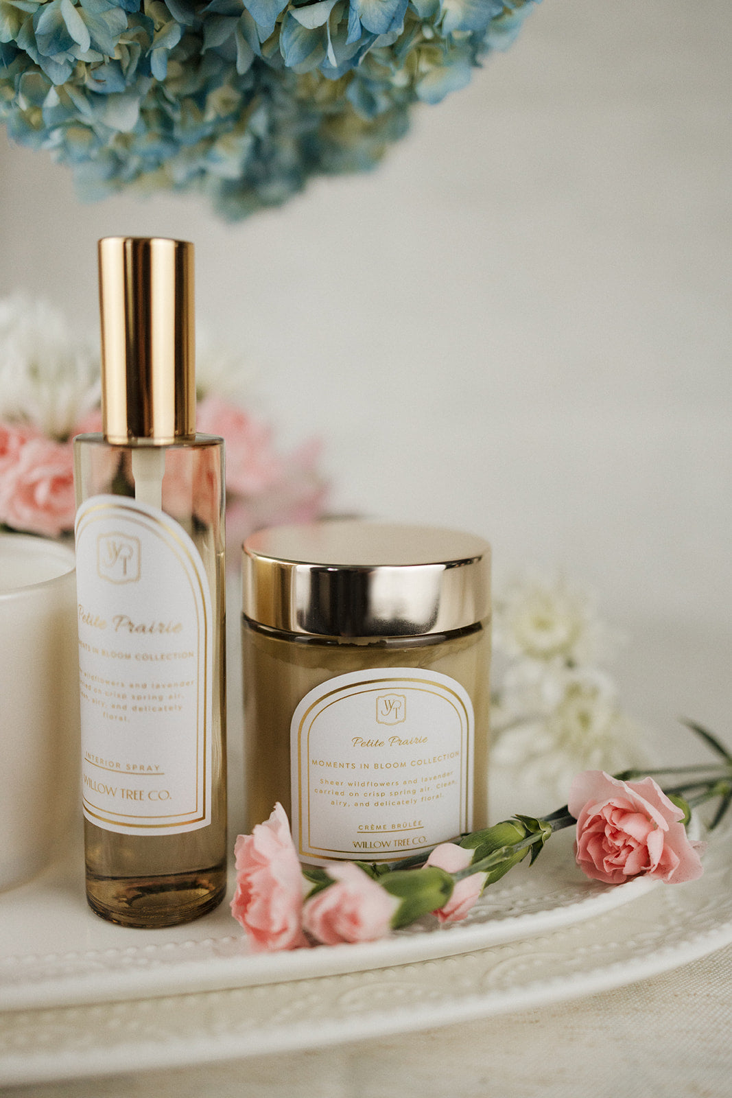 Interior spray and b ody cream with gold caps on a white surface with flowers in the background