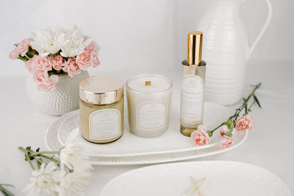 Candle, body cream, and interior spray set on a white tray with flowers in the background