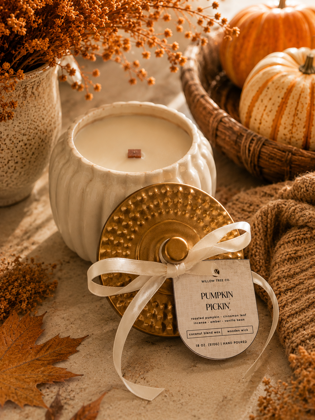 A styled product photo of a 'Pumpkin Pickin' scented candle by Willow Tree Co. The candle is shown in a white ribbed ceramic jar alongside its gold textured lid, which is tied with a white satin ribbon and a paper tag.