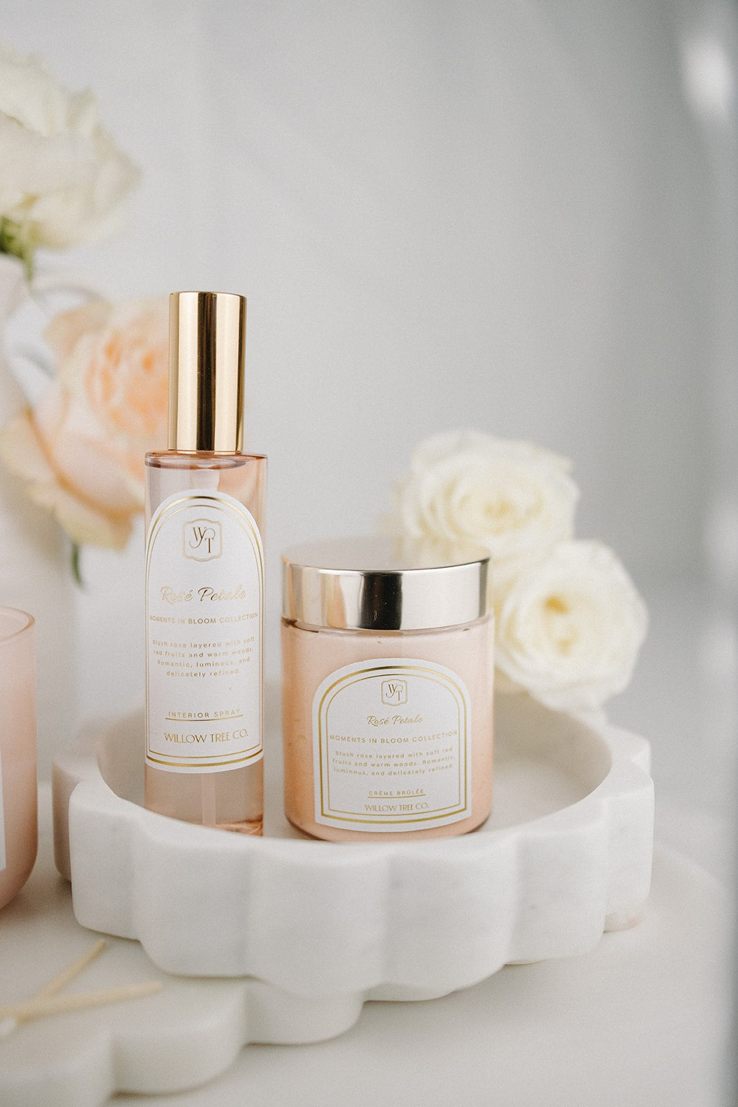 Interior spray and body cream with gold caps on a white dish with flowers in the background