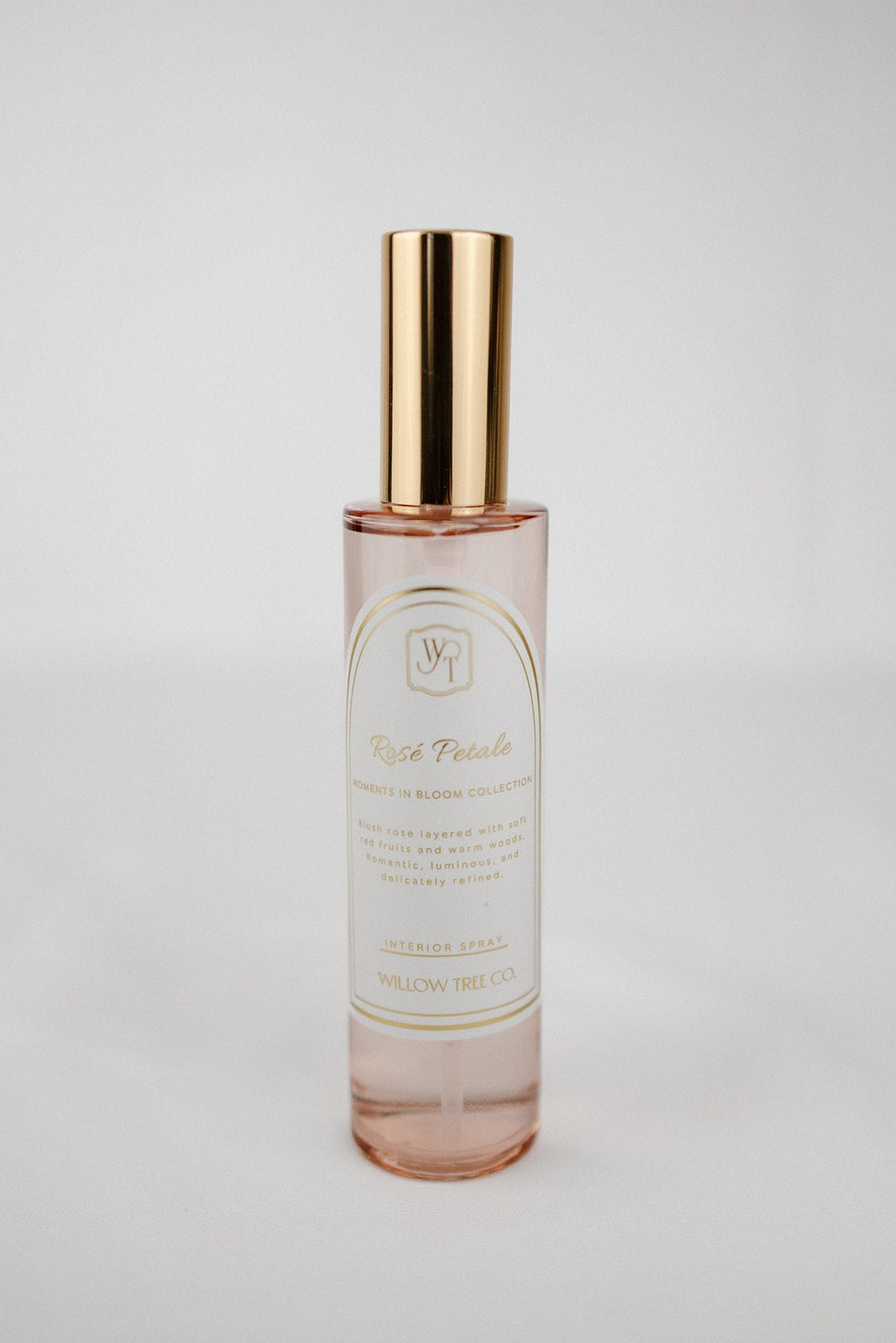 Pink interior spray bottle with gold cap and white label on a light gray background