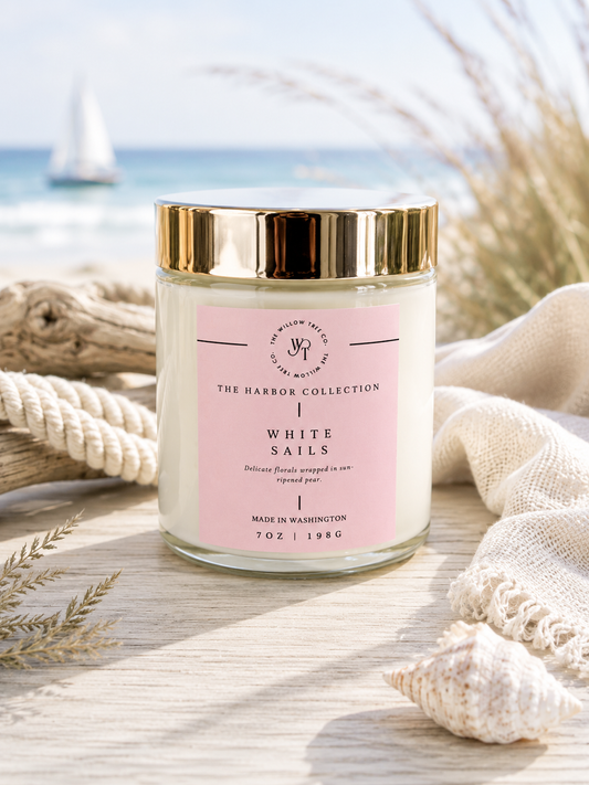 Luxury coastal candle with a soft blush pink label styled beside driftwood, rope, and seashells with an airy ocean backdrop.