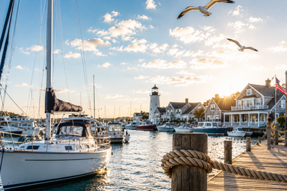 Harbor scene with boats, a lighthouse, and houses under a blue sky with clouds.